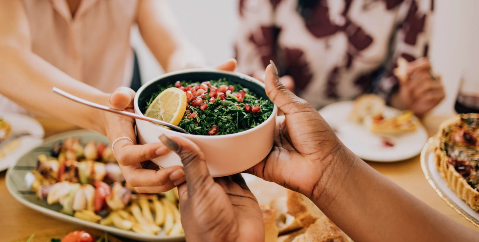 Hands passing a bowl of fresh salad.